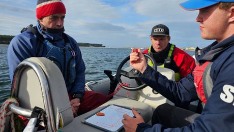 An instructor briefing two students at the helm of a powerboat