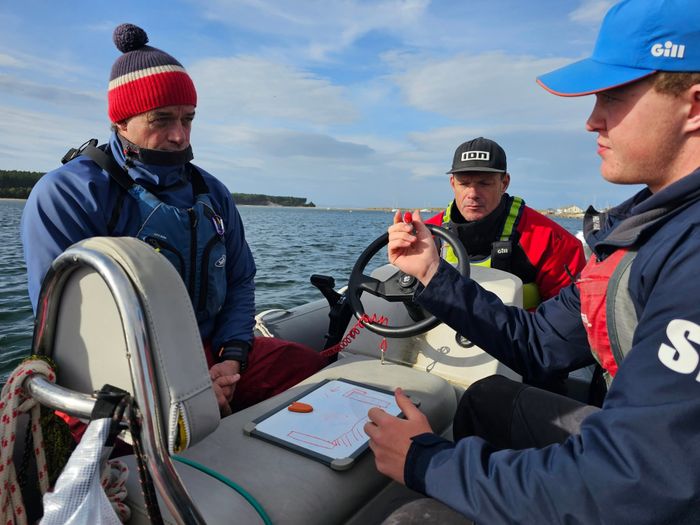 An instructor briefing two students at the helm of a powerboat