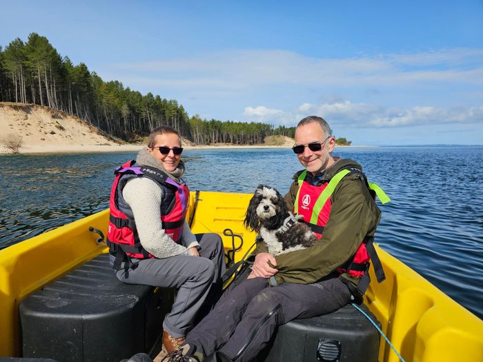 Two passengers and a dog crossing the bay with the Culbin dunes behind